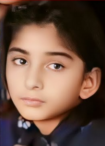 Photo of a young girl with light-brown skin, wavy dark hair, and dark-brown eyes, with a solemn expression on her face.