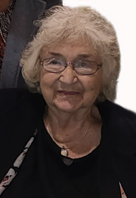 Photo of an elderly woman with white hair. She has light, wrinkled skin, and she is wearing glasses, a black top, and a necklace with a white stone.