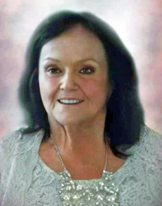 Photo of a middle-aged woman with pale skin and rosy cheeks, smiling for the camera. She is wearing a light-blue flowered blouse, and she has shoulder-length brown hair. 