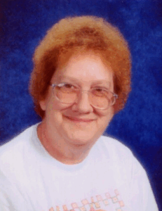 Portrait photo of an older woman with pale skin and a halo of red hair; she is wearing glasses and a white shirt.