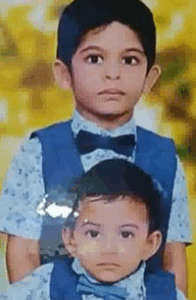 Photo of two Indian boys, one older than the other, in matching outfits consisting of a blue vest, light-blue flowered shirt, and blue bow tie. They both have light-brown skin and black hair, and their expressions are solemn.