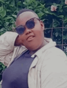 Photo of a heavyset young woman with brown skin and a buzz cut, wearing sunglasses, a gray shirt, and a khaki cardigan.