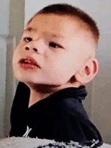 Photo of a young boy with pale skin and short auburn hair. He is wearing a black shirt. His chin is tilted upward.