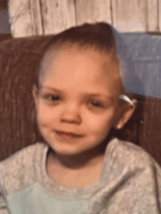 Photo of a small girl with pale skin and dark-blond hair pulled away from her face. She is wearing a baggy off-white sweatshirt.