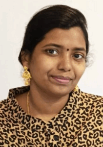 Indian woman with light-brown skin, dark-brown straight hair tied back in a ponytail, and gold earrings. She has a bindi on her forehead, and is wearing a jaguar-print shirt and thin gold necklace.