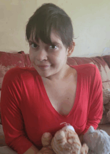 Photo of a young woman with short, straight brown hair and lightly tanned skin, wearing a red V-neck long-sleeved shirt and holding two stuffed animals in her arms.