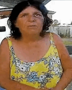 Photo, somewhat distorted, of a middle-aged woman with tanned skin and short brown hair, wearing a yellow tank top.