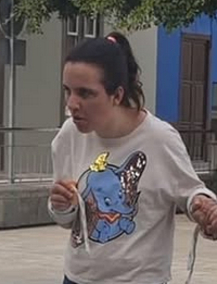 Photo of a young woman with light skin and dark hair in a ponytail. She is looking away from the camera, and holding someone's hand off-frame. She is wearing a white shirt with Dumbo the elephant on the front.