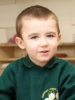 Photo of a boy in a green polo shirt. He has pale skin and short, light-brown hair.