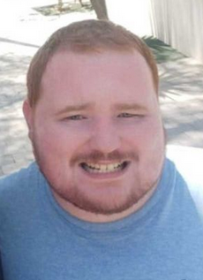 Photo of a man with pink skin, a round face, and strawberry-blond hair. He has a neatly cut mustache and beard. He is smiling, his eyes squeezed nearly shut.