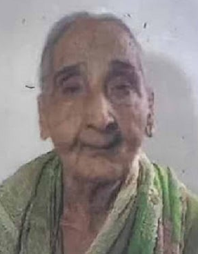 Photo of an elderly Indian woman with light-brown skin and white hair, wearing a green saree. 